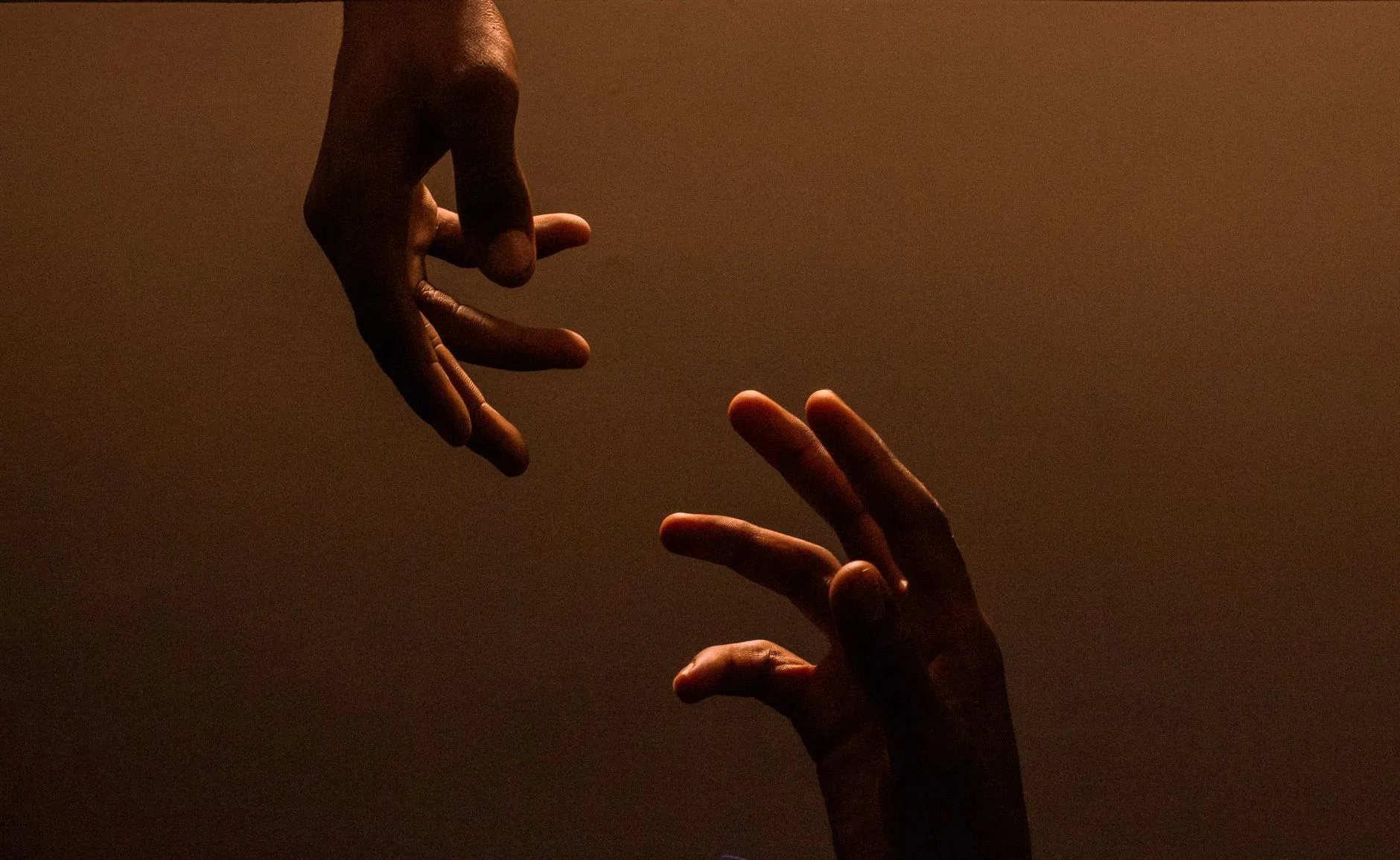 Two hands reaching toward each other against a dark, warm background